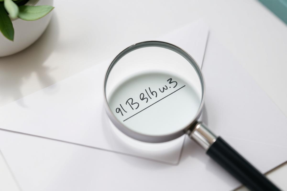 Loupe posée sur une enveloppe blanche manuscrite, lumière naturelle et plante verte